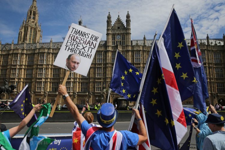 A pro-EU demonstrator holds a placard bearing an image of Russia's President Vladimir Putin, as others wave flags during a protest against Brexit, outside of the Houses of Parliament in central London on June 11, 2018. - After a rollercoaster week of Brexit rows within her government and with Brussels, British Prime Minister Theresa May will on Tuesday seek to avoid another setback in a long-awaited showdown with parliament. MPs in the House of Commons will vote on a string of amendments to a key piece of Brexit legislation that could force the government's hand in the negotiations with the European Union. (Photo by Daniel LEAL-OLIVAS / AFP)        (Photo credit should read DANIEL LEAL-OLIVAS/AFP/Getty Images)