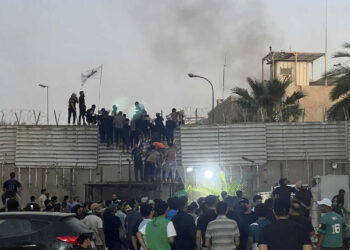 CORRECTS SECOND SENTENCE - Protesters scale a wall at the Swedish Embassy in Baghdad Thursday, July 20, 2023. Protesters angered by the planned burning of a copy of the Quran stormed the embassy early Thursday, breaking into the compound and lighting a small fire. (AP Photo/Ali Jabar)