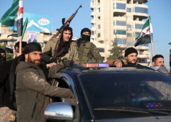 Anti-government fighters brandish their guns as they ride a vehicle in Syria's northern city of Aleppo on November 30, 2024. Jihadists and their Turkish-backed allies breached Syria's second city of Aleppo on November 29, as they pressed a lightning offensive against forces of the Iranian- and Russian-backed government. (Photo by Omar HAJ KADOUR / AFP) (Photo by OMAR HAJ KADOUR/AFP via Getty Images)