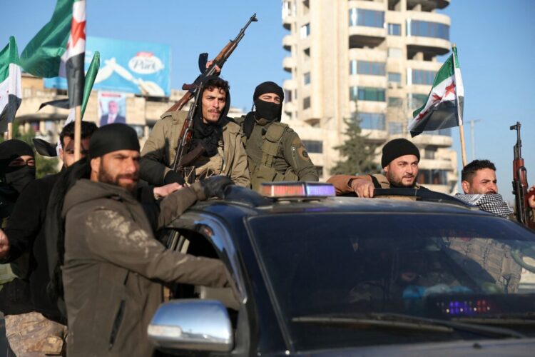 Anti-government fighters brandish their guns as they ride a vehicle in Syria's northern city of Aleppo on November 30, 2024. Jihadists and their Turkish-backed allies breached Syria's second city of Aleppo on November 29, as they pressed a lightning offensive against forces of the Iranian- and Russian-backed government. (Photo by Omar HAJ KADOUR / AFP) (Photo by OMAR HAJ KADOUR/AFP via Getty Images)